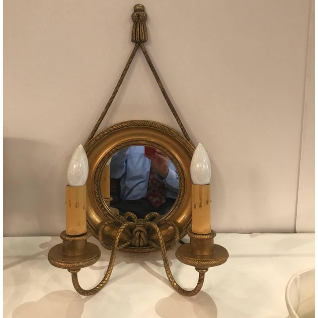 A pair of giltwood and gilt metal wall sconces with mirrored backs. The round framed backs with mirrors with rope style...