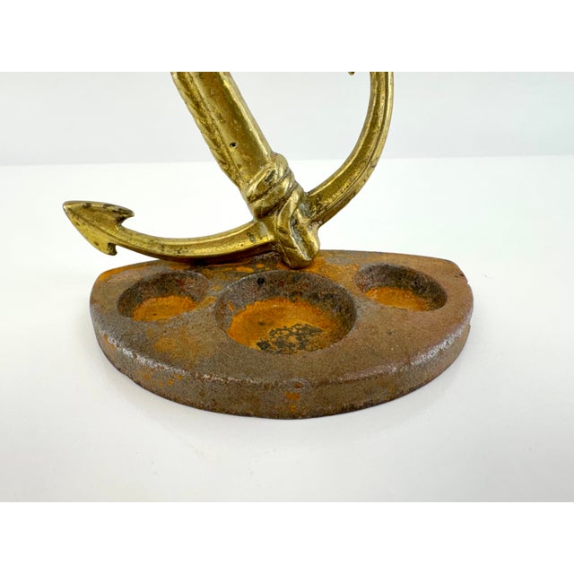 A vintage brass anchor mounted atop a heavy cast iron base, creating a distinctive nautical desk accessory with timeless...