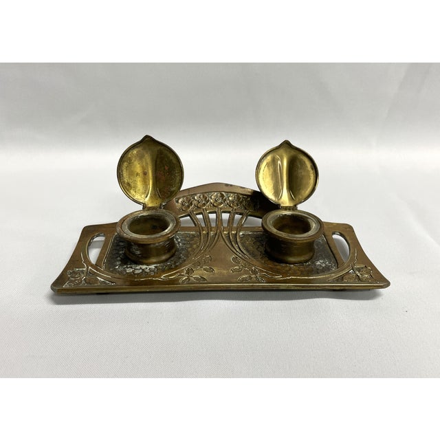 An antique brass double inkwell by Geschutzt in the art nouveau style. The inkwell displays an engraved floral and leaf...