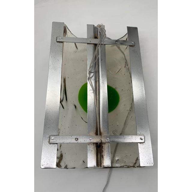 Wall lamp with rectangular satin metal base on which a thick and transparent glass with an irregular surface is mounted,...