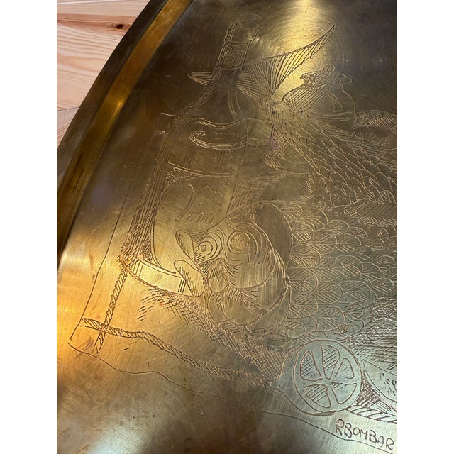 Decorative brass tray by Remo Bombarieri, featuring an engraved still-life composition of fish, a wine bottle, a covered...