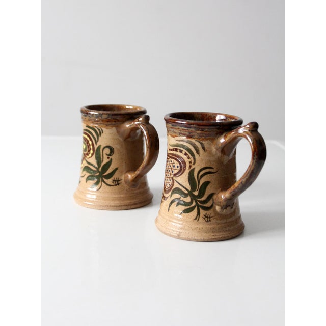 This matched pair of vintage hand painted studio pottery mugs features expressive floral designs and rich, earthy glazes...