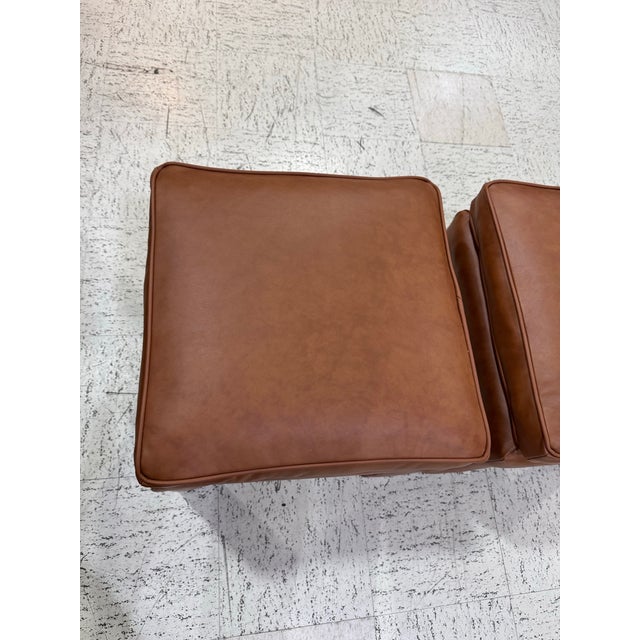 A handsome pair of vintage ottomans, newly reupholstered in genuine leather in a rich caramel brown. The clean,...