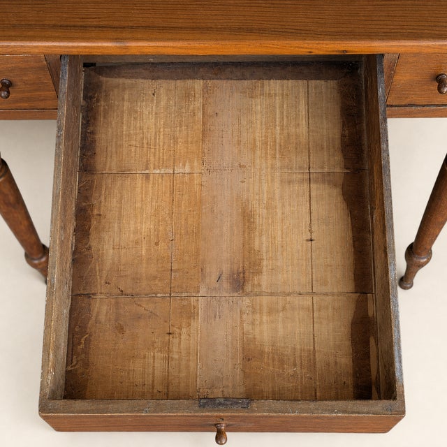 An antique walnut writing desk with a richly grained rectangular top and three drawers across the front. A broad center...