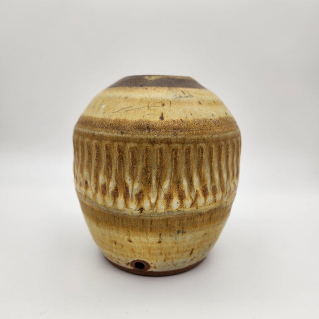 Stoneware vase with carved vertical fluting band, layered amber and brown ash glaze, dark-glazed rim, drainage hole, and...