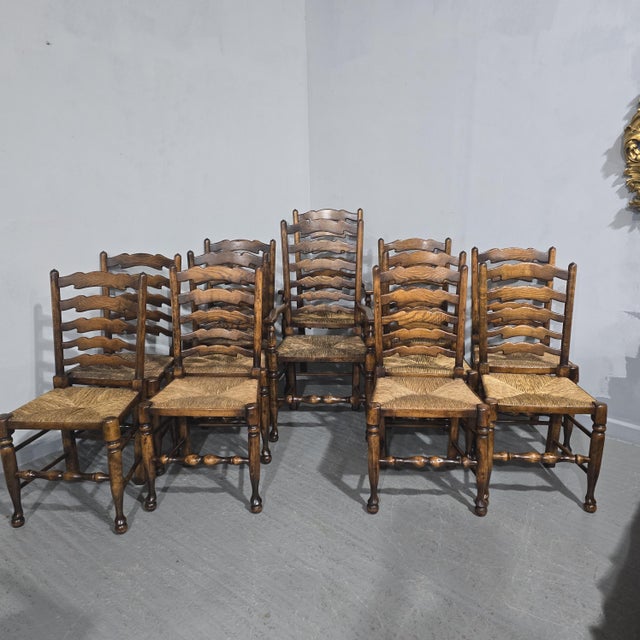 A super set of twelve oak and rush seated Lancashire ladder backed dining chairs, ten singles and two carvers, in...