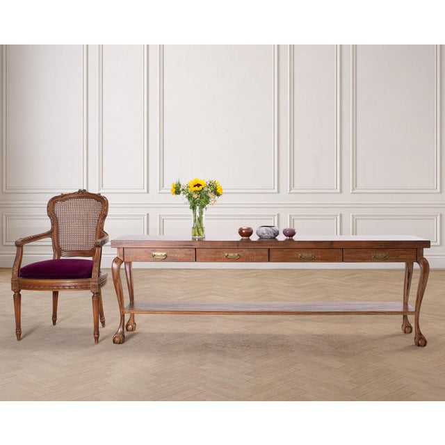 A charming weathered long walnut console or sofa table crafted in an English Queen Anne, or Country English style. The...