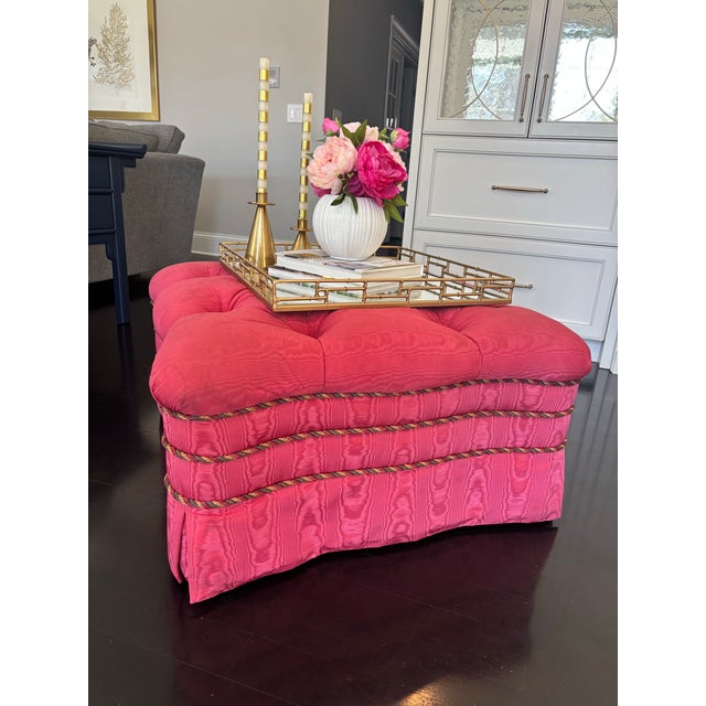 Offered is an upholstered skirted tufted button ottoman set on rolling wheels with rope details. This piece is unmarked.