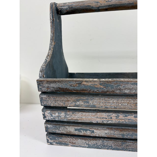 Vintage wooden tool caddy with a slatted body, solid wood sides, and a fixed carrying handle. The blue-gray painted finish...