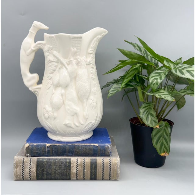 Captivating, sculptural ceramic pitcher in a warm cream-toned glaze, featuring an elaborate relief of hanging game birds...