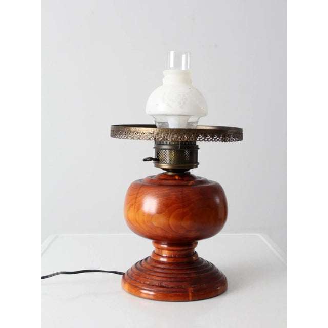 This is an electrified antique oil lamp. Featuring a stunning turned wood base, the table lamp has a decorative brass top...