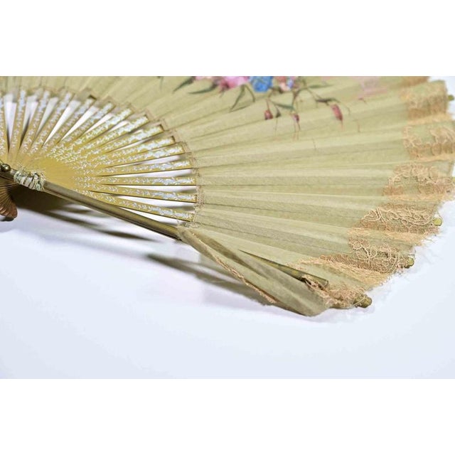 A charming hand-painted folding fan featuring a finely pleated silk leaf delicately bordered with an appliqué of peach-...