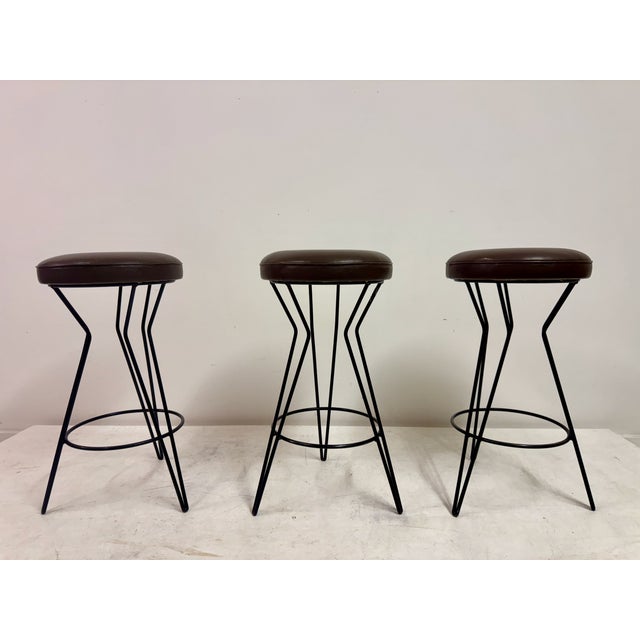 A set of three mid to late century bar stools, combining light industrial construction with clean, modern lines. Each...