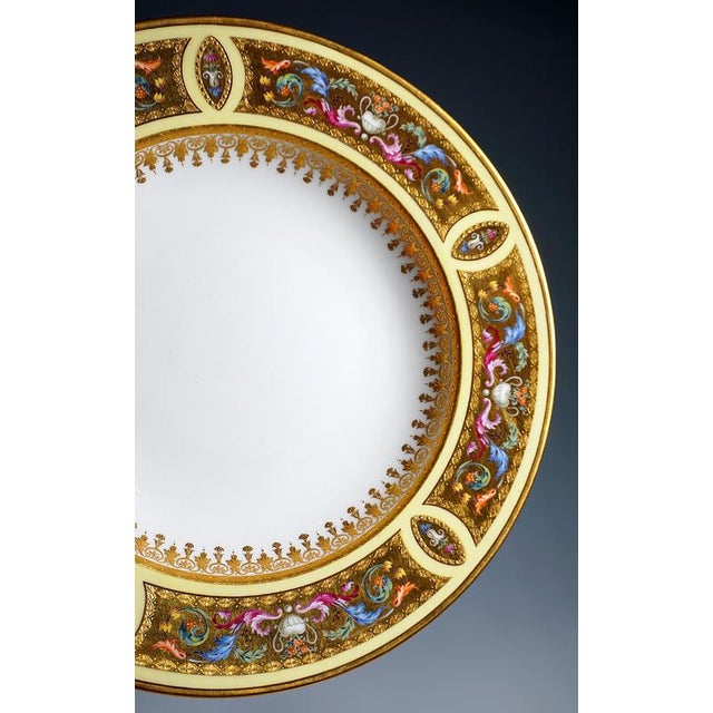 A porcelain plate decorated with the finest painting: border with a lemon-yellow background behind five large, curved gold...