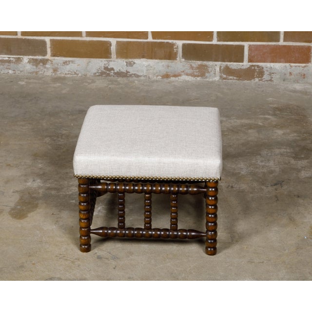 An English bobbin stool from the 19th century with linen upholstered seat and brass nailhead trim. Bringing timeless charm...