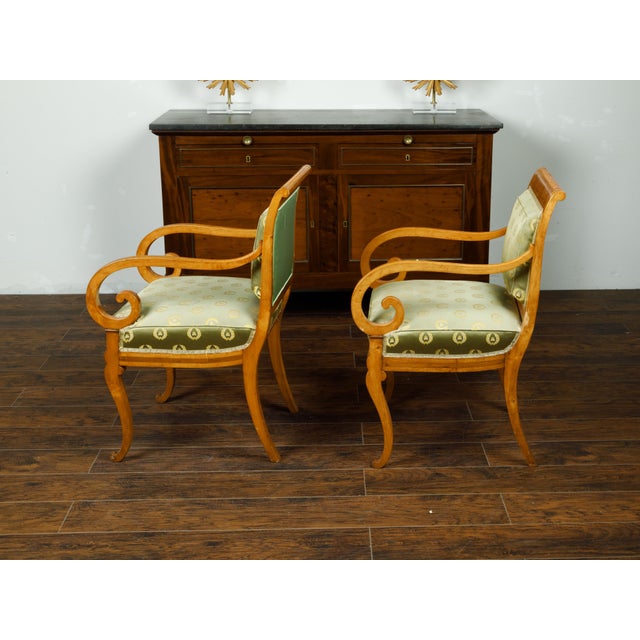A pair of English Regency walnut armchairs from the mid 19th century, with large scrolling arms and green upholstery....