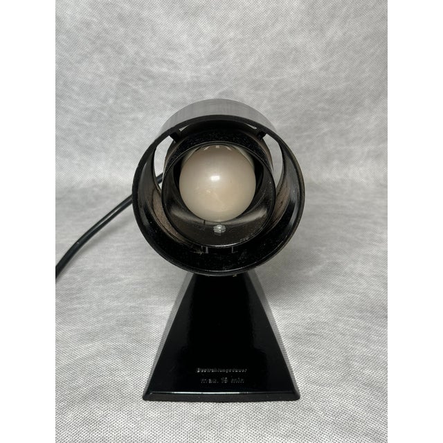 Industrial spotlight lamp with an adjustable shade mounted on a plastic base. Minimalist and functional design typical of...