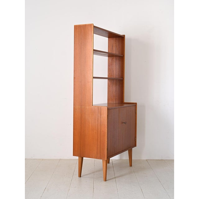 Scandinavian teak bookcase from the 1960s. The lower part has a large compartment closed by two hinged doors, while the...