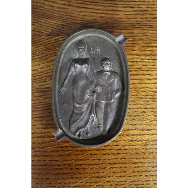 Striking Art Deco brass ashtray with a playful, risqué figural design. The oval tray is cast with stylized male and female...