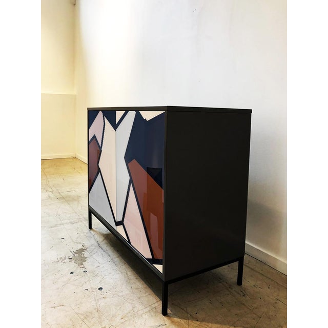 The Strata Cabinet design is a bold, modern piece that merges art and design, featuring an abstract geometric composition...