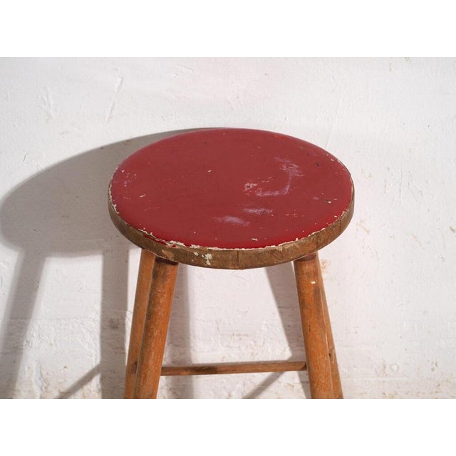This antique wooden stool is a three-legged seat with a round seat and turned splayed legs joined by stretchers. It...