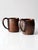This pair of vintage copper mugs showcases classic rounded silhouettes and riveted handles, finished in a rich, aged...