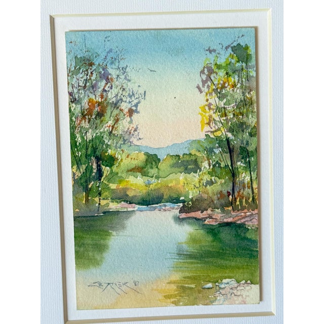A lovely and beautifully executed original watercolor landscape of a reflective river and vibrant green trees and...