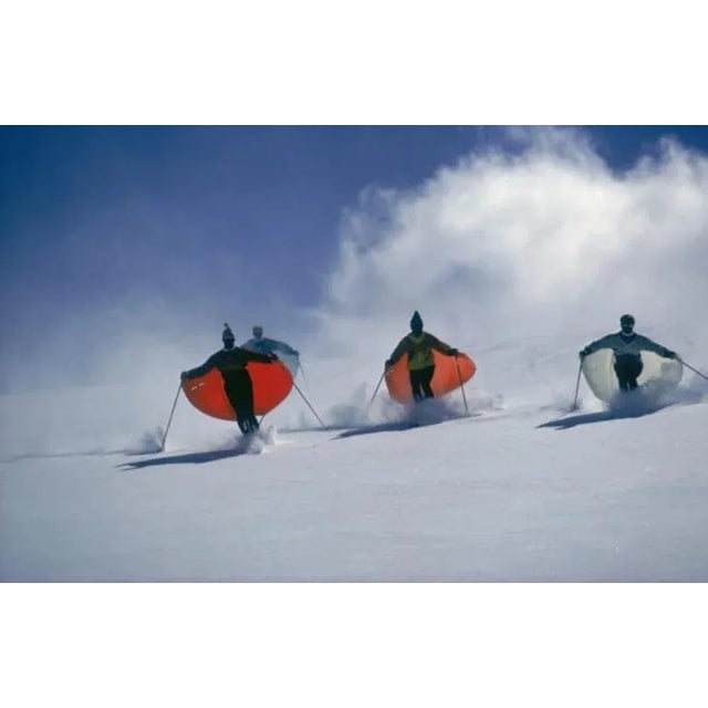 Caped Skiers 1975 by Slim Aarons Slim Aarons Limited Estate Edition Led by skimaster Stein Eriksen, skiers ‘sail’ down a...