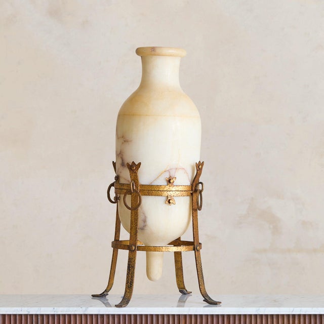 A tall French alabaster vase elevated within a gilt metal stand, likely dating to the early 20th century. Carved from...
