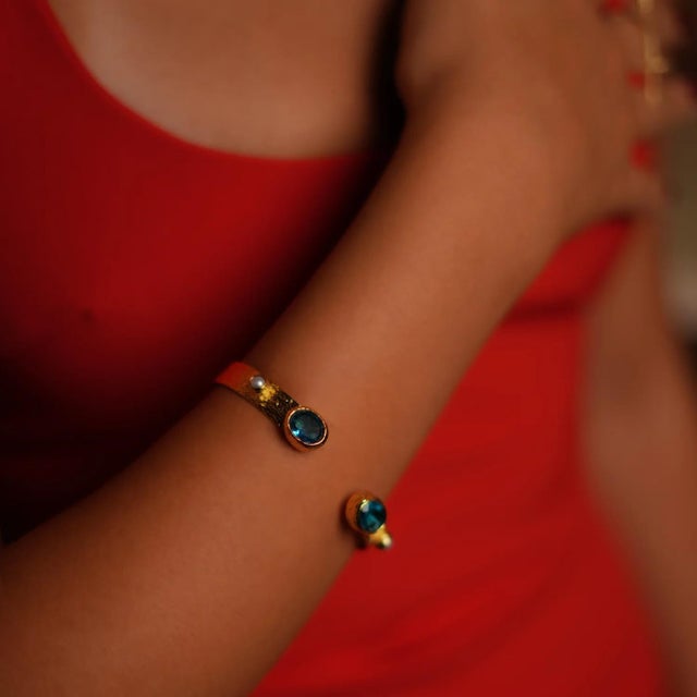 Embrace regal elegance with the Cleopatra Blue Topaz & Pearl Adjustable Gold Cuff Bracelet. This exquisite cuff, plated in...