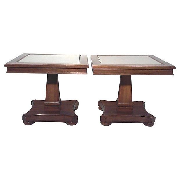 A pair of wood and travertine Neo-Classical end tables with pedestal bases. The natural stone tops are in a neutral, off...