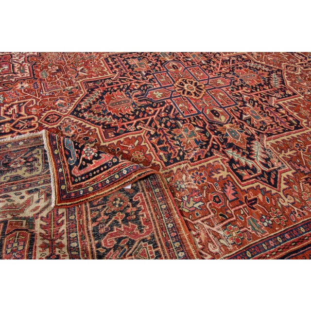 This vintage Persian wool rug, featuring a rust-colored field, showcases a striking dark blue border adorned with vibrant...