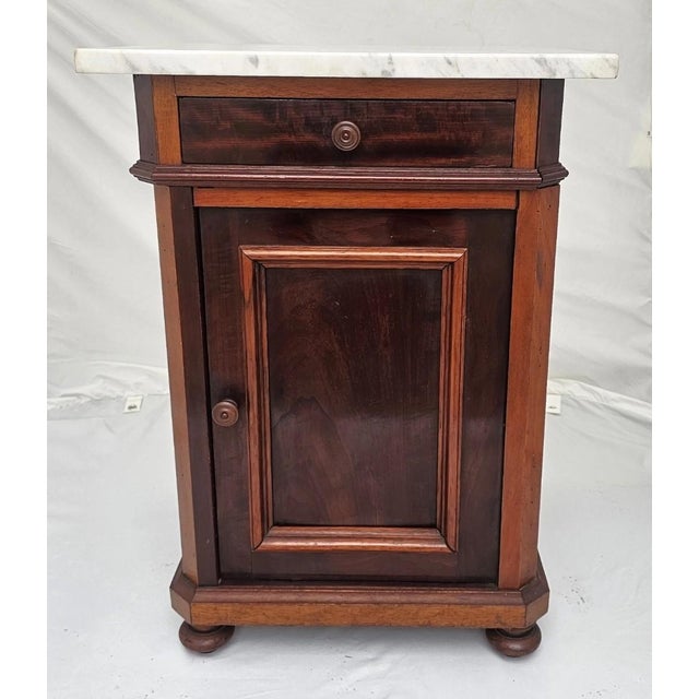 A charming and highly functional American Victorian marble top nightstand, dating to the 1890s, offering a beautiful blend...