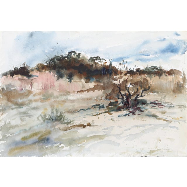 Emerging from the dunes along the border of the beach, grasses sway with the ocean wind as the sand blows over the beach...