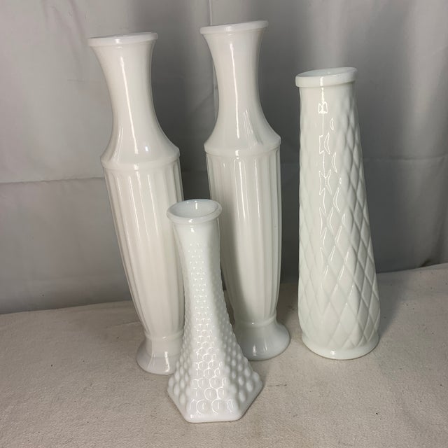 A charming collection of vintage mid-century white milk glass bud vases featuring classic fluted, hobnail, and diamond-...