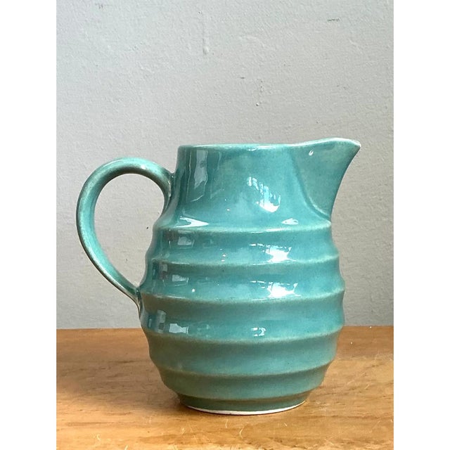 This vintage aqua ribbed ceramic pitcher presents a charming, rounded silhouette, with a full, bulbous belly that narrows...