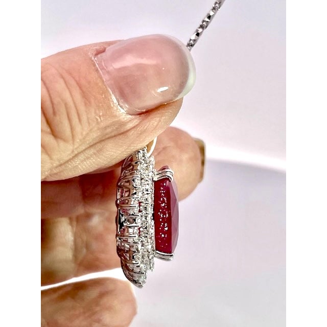 A stunning pendant necklace featuring a large, oval-cut ruby as its centerpiece, displaying a rich, vivid crimson-red hue...