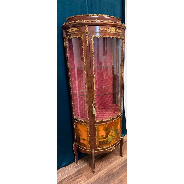 An elegant French Louis XVI-style vitrine cabinet featuring a graceful curved silhouette, richly toned mahogany or walnut-...