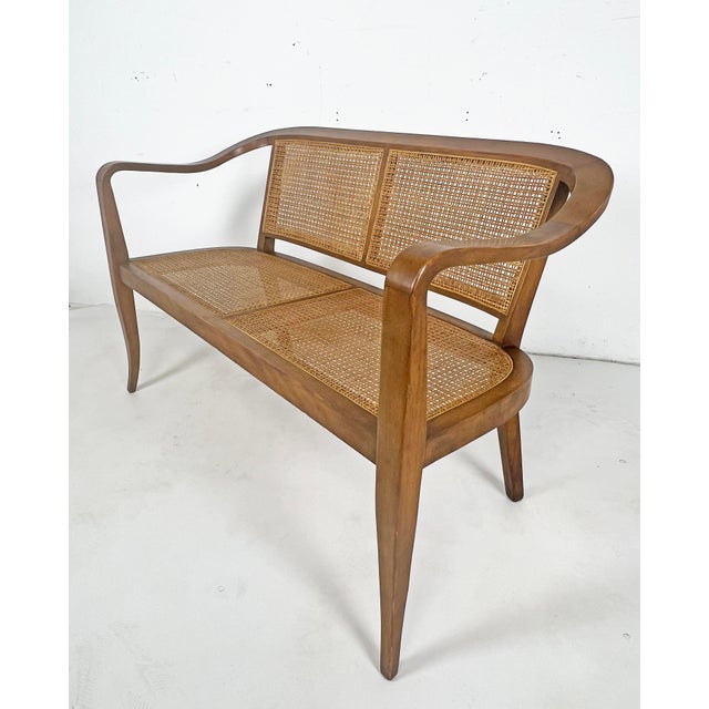A curvacously carved and hand-caned settee in the manner of Edward Wormley for Dunbar, circa 1950s.