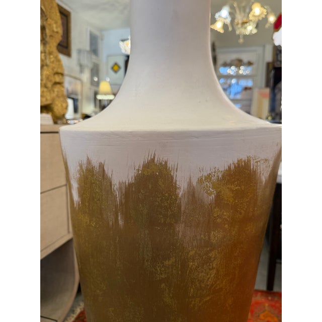 Tall vessel or urn handmade with plaster and other sculpting materials. The vessel is white with gold leaf painted and...