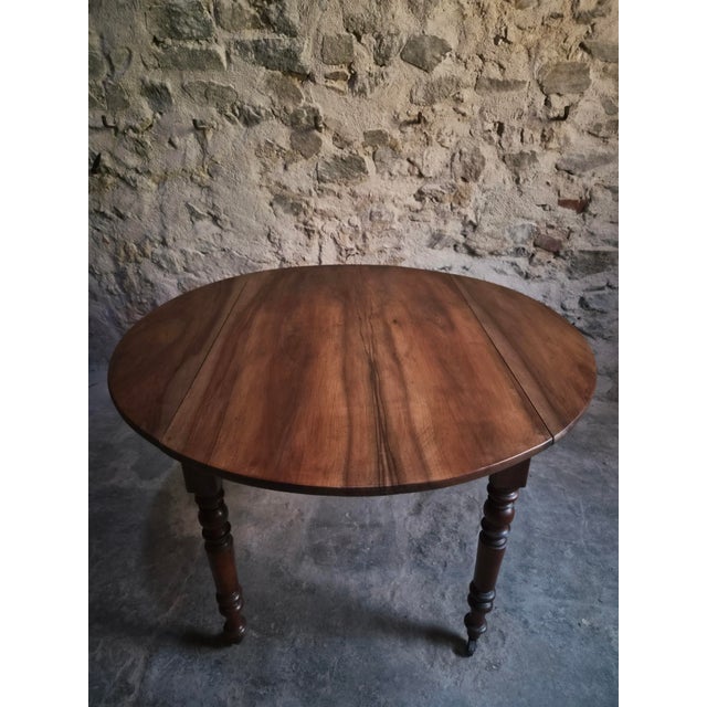 Antique walnut drop-leaf dining table from France, dating from around 1900. The table has a round top with two hinged...