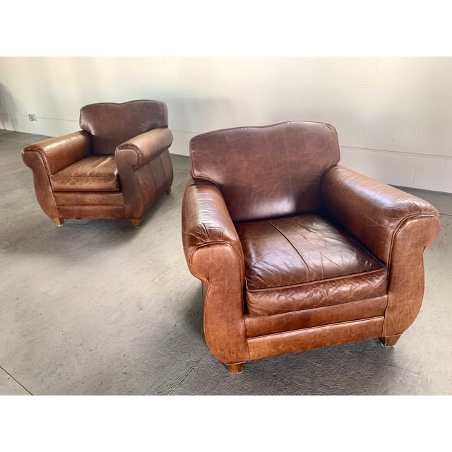 A stunning pair of vintage-inspired French Art Deco leather club chairs. Crafted in a classic Parisian silhouette, these...