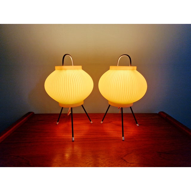 Pair of lamps with a black lacquered metal tripod base and a pale green pleated celluloid shade, 1960s. They are in superb...
