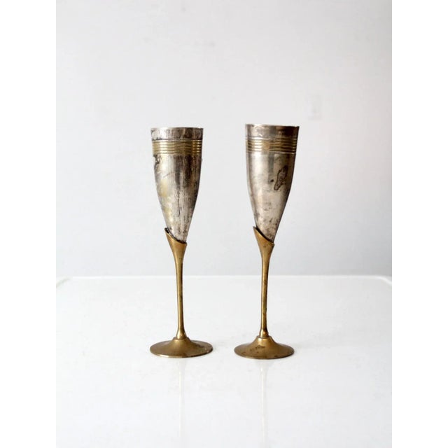 A pair of vintage champagne flutes crafted in brass and silver plate, each featuring a distinctive ribbed chalice form....