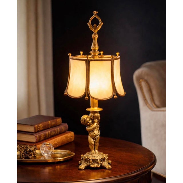 Stunning vintage Hollywood Regency table lamp featuring an ornate brass cherub base and original slag glass panel shade....