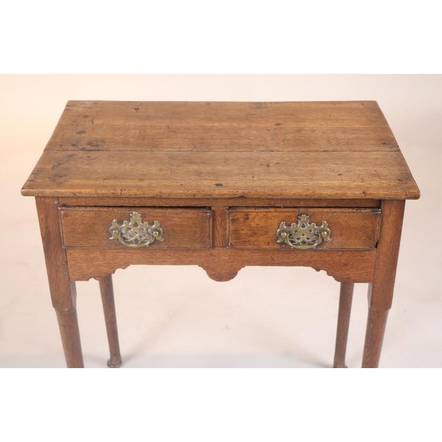 A small George I oak side or dressing table with two drawers, brass bail pulls, pierced escutcheons, shaped apron and...