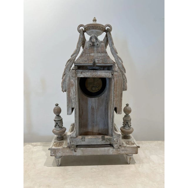 Very ornate white washed wood mantle clock with gold details. The face is behind a functional glass door with latch. The...