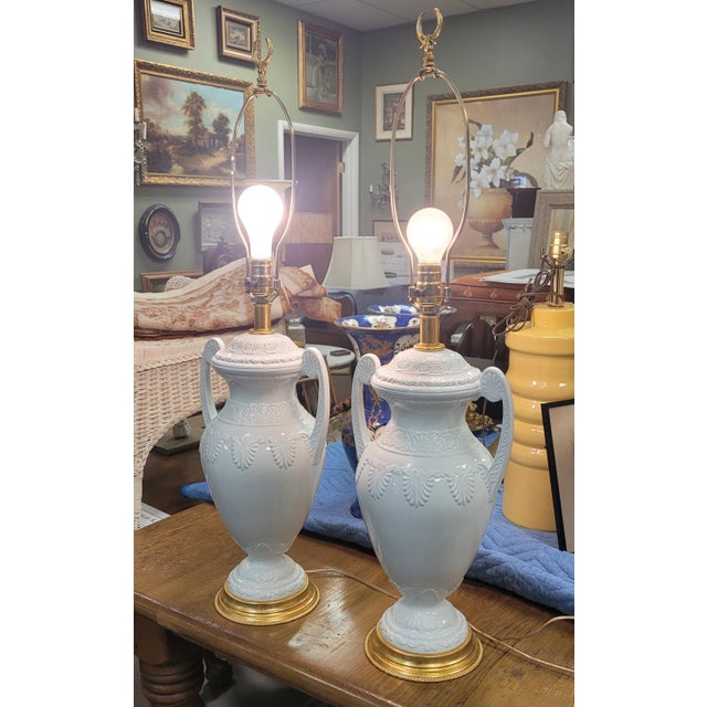 An elegant pair of porcelain and gilt brass table lamps in the Regency style. Each lamp features bone white porcelain urn...