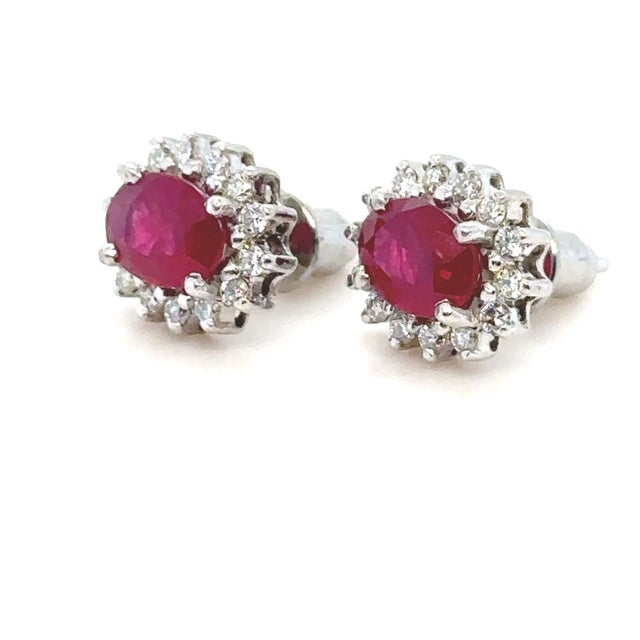 A Pair Of Oval Ruby Oval Cluster Stud Earrings, claw set in 18ct white gold within a border of 14 round brilliant cut...