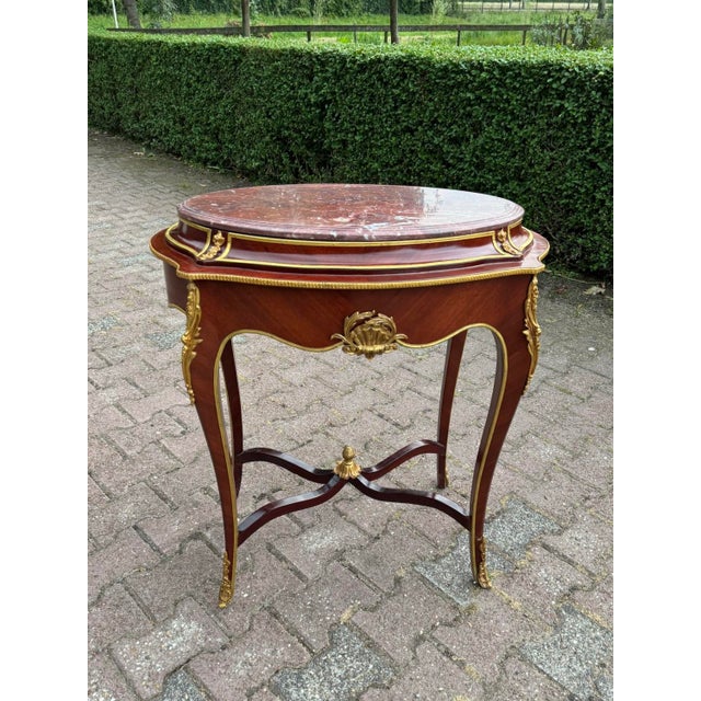 This refined early 1900s French Louis XVI–style side table combines richly toned mahogany with decorative gilt-bronze...